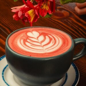 A cup of artistic floral latte with red flower accents on a wooden table.