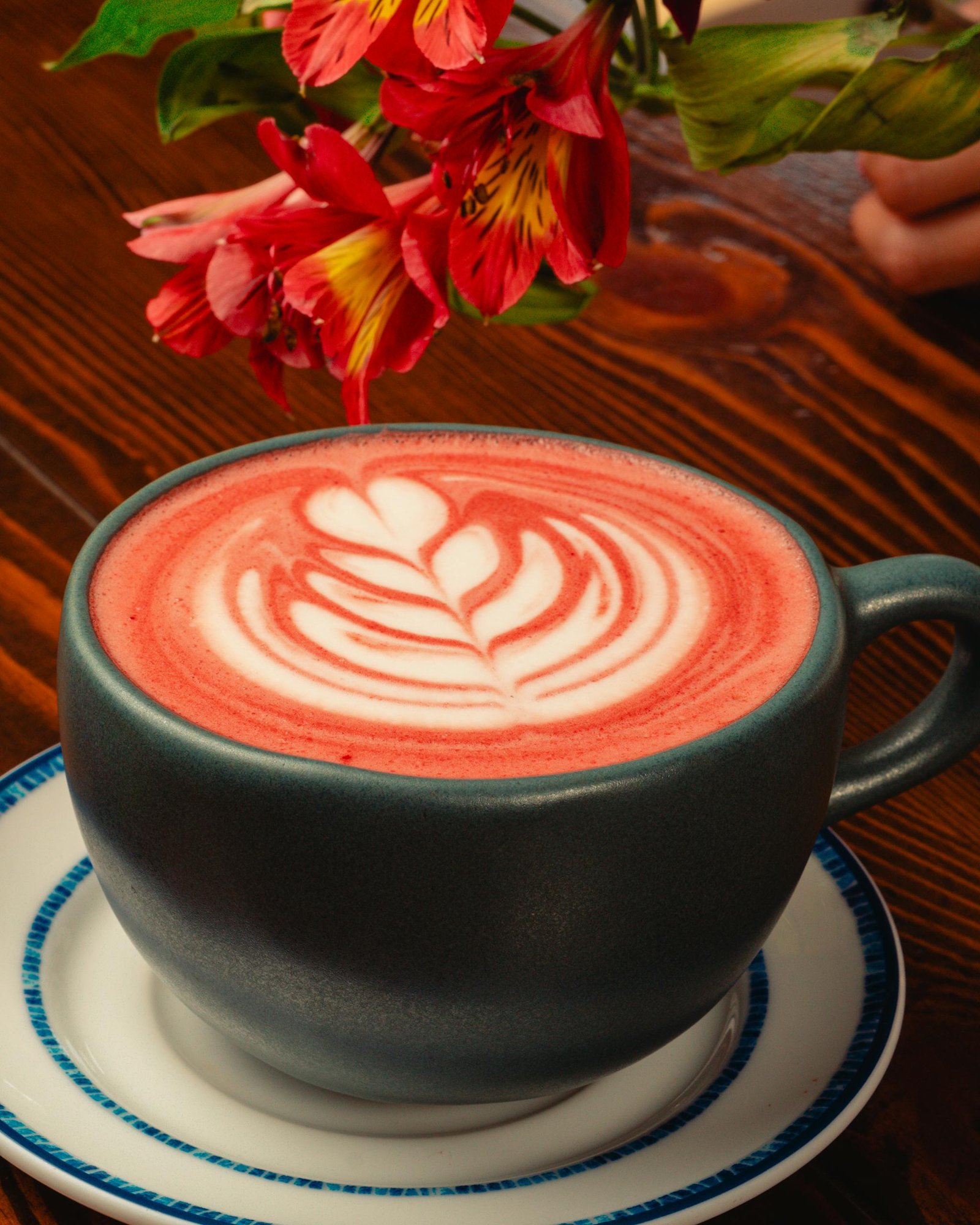 A cup of artistic floral latte with red flower accents on a wooden table.
