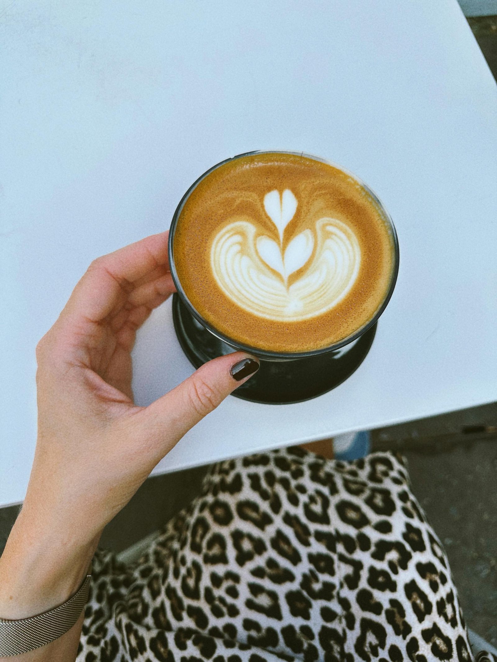 A hand holding a latte with frothy art, capturing a cozy cafe moment.