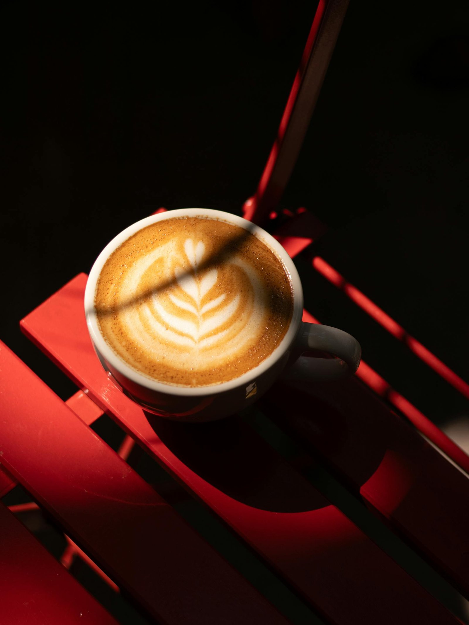 Capture of a beautifully crafted latte with intricate foam art on a vibrant red table.